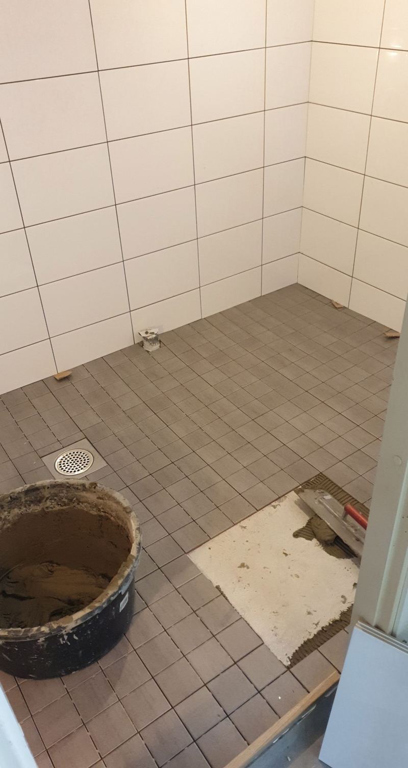 Suihkutilan seinillä valkoinen laatta ja lattialla harmaat pienet laatat
